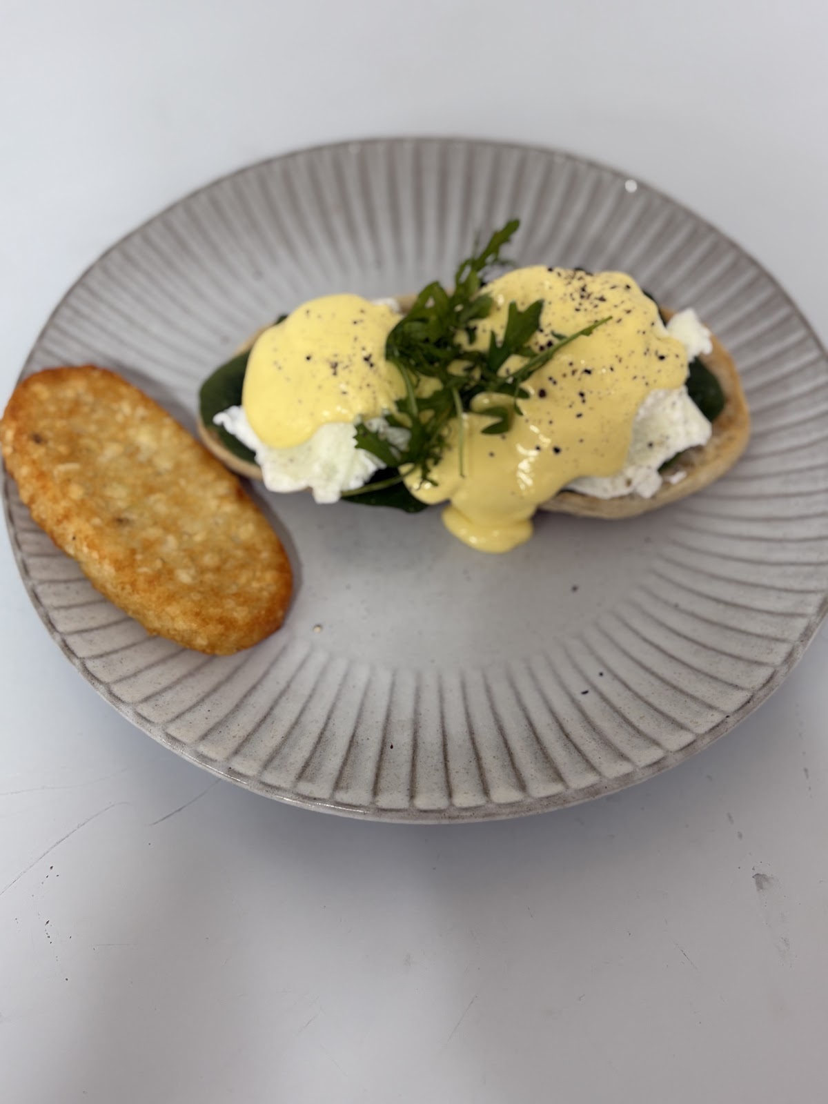 Eggs benedict with a hash brown on a grey ribbed plate