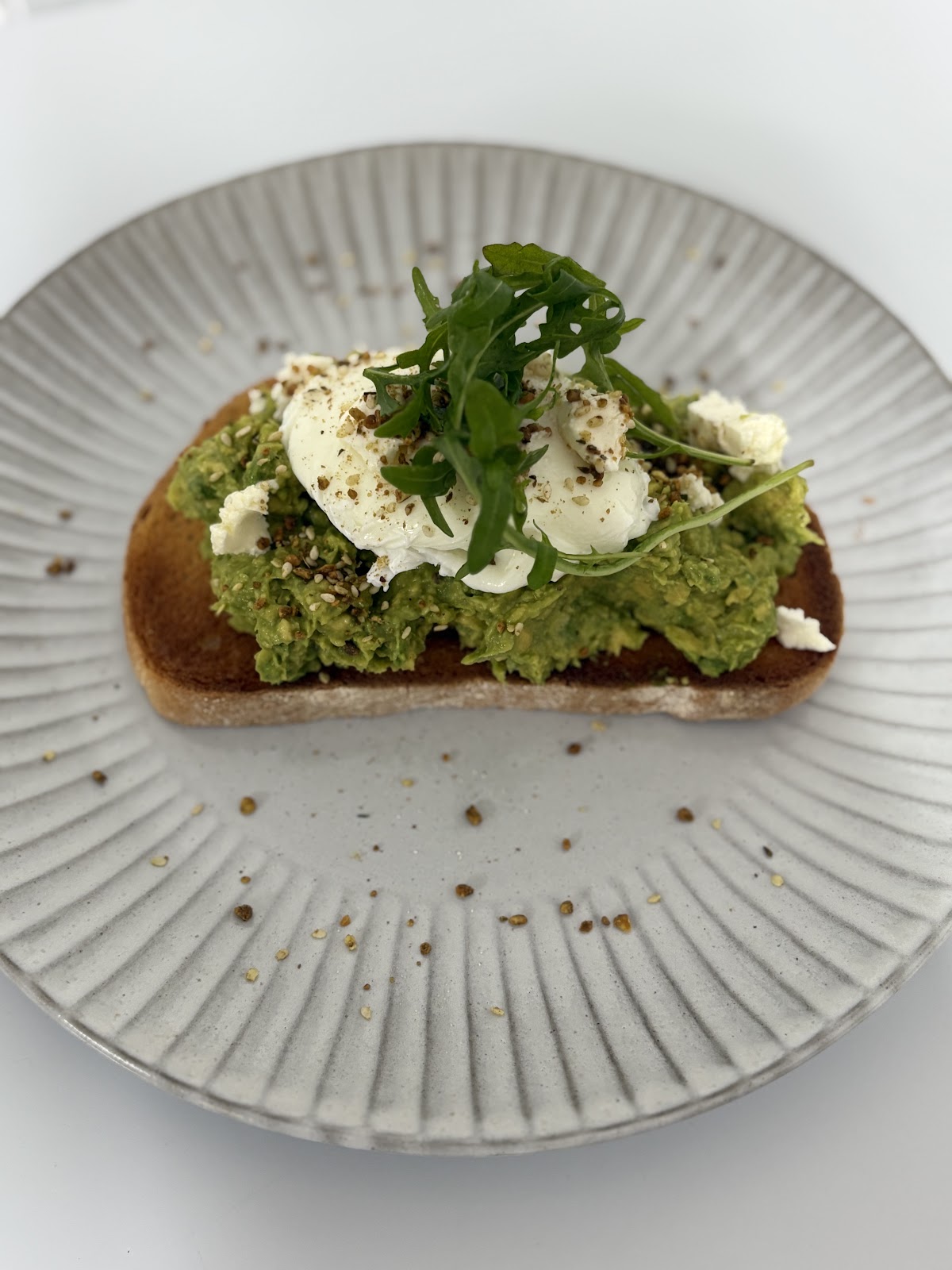Smashed avocado on toast topped with a poached egg and rocket